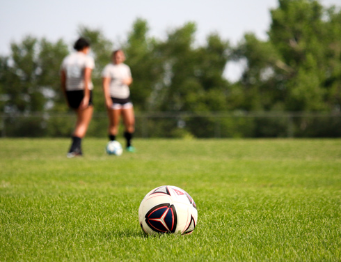 football on pitch, two players in distance chatting